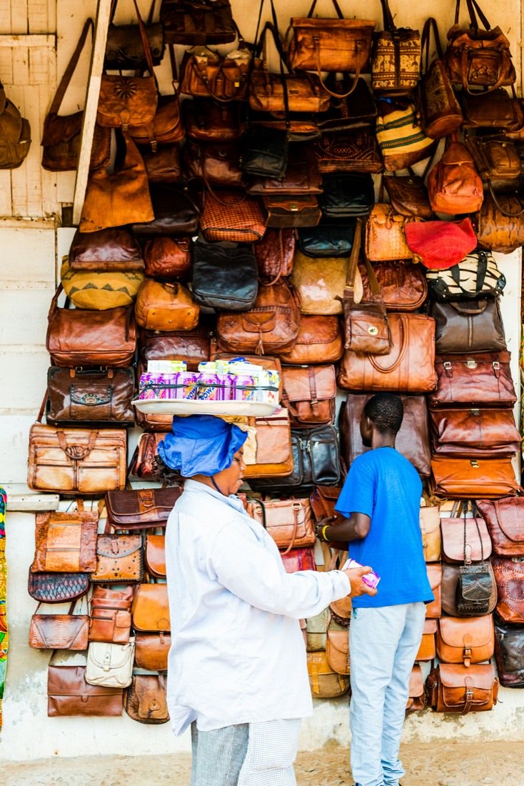 Two men at a stall with a wall of leather bags
